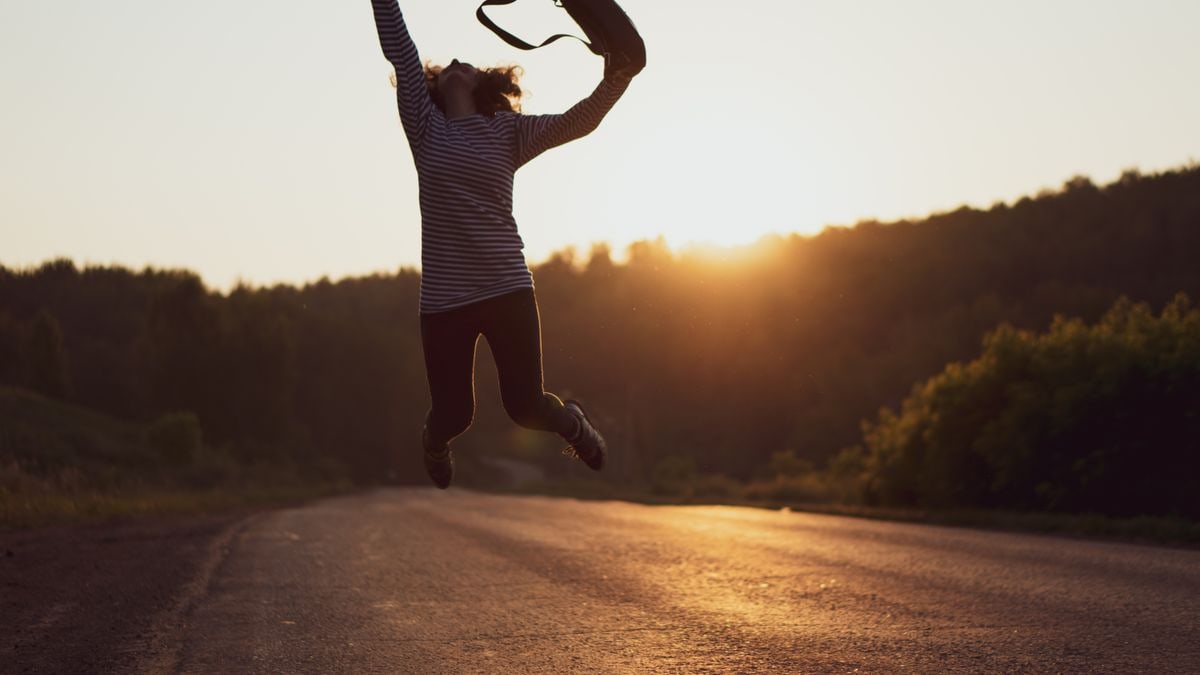 Silhouette of a woman jumping joyfully on an open road at sunset, embodying freedom and adventure.